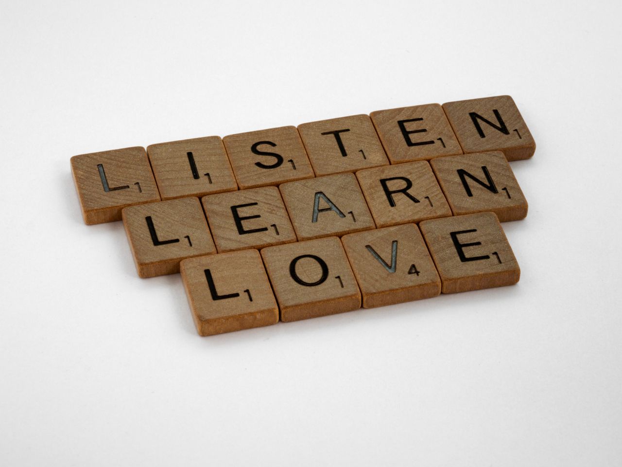 Scrabble tiles arranged to spell Listen, Learn, Love on a white background.